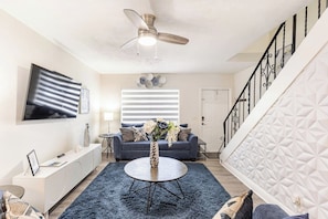 A living room with a ceiling fan, a flat-screen TV, a sofa, a coffee table, and a staircase. - Cozy Retreat | Beach, Airport & Cruise Port (Fort Lauderdale)