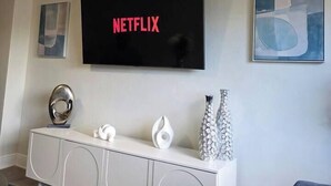 Een woonkamer met een flatscreen televisie aan de wand bevestigd, een witte entertainmentkast eronder en abstracte kunstwerken op de muren.