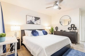 Ein modernes Schlafzimmer mit Bett, Nachttischen, Schreibtisch, Kommode, Deckenventilator, Spiegel und einem Wandbild.