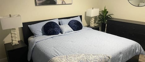 A bed with a patterned throw, two bedside lamps, a wall-mounted abstract painting, and a round mirror.