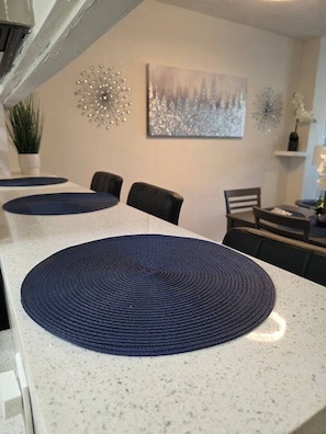 A dining area with a long table, dark placemats, and a painting on the wall. - Cozy Retreat | Beach, Airport & Cruise Port (Fort Lauderdale)