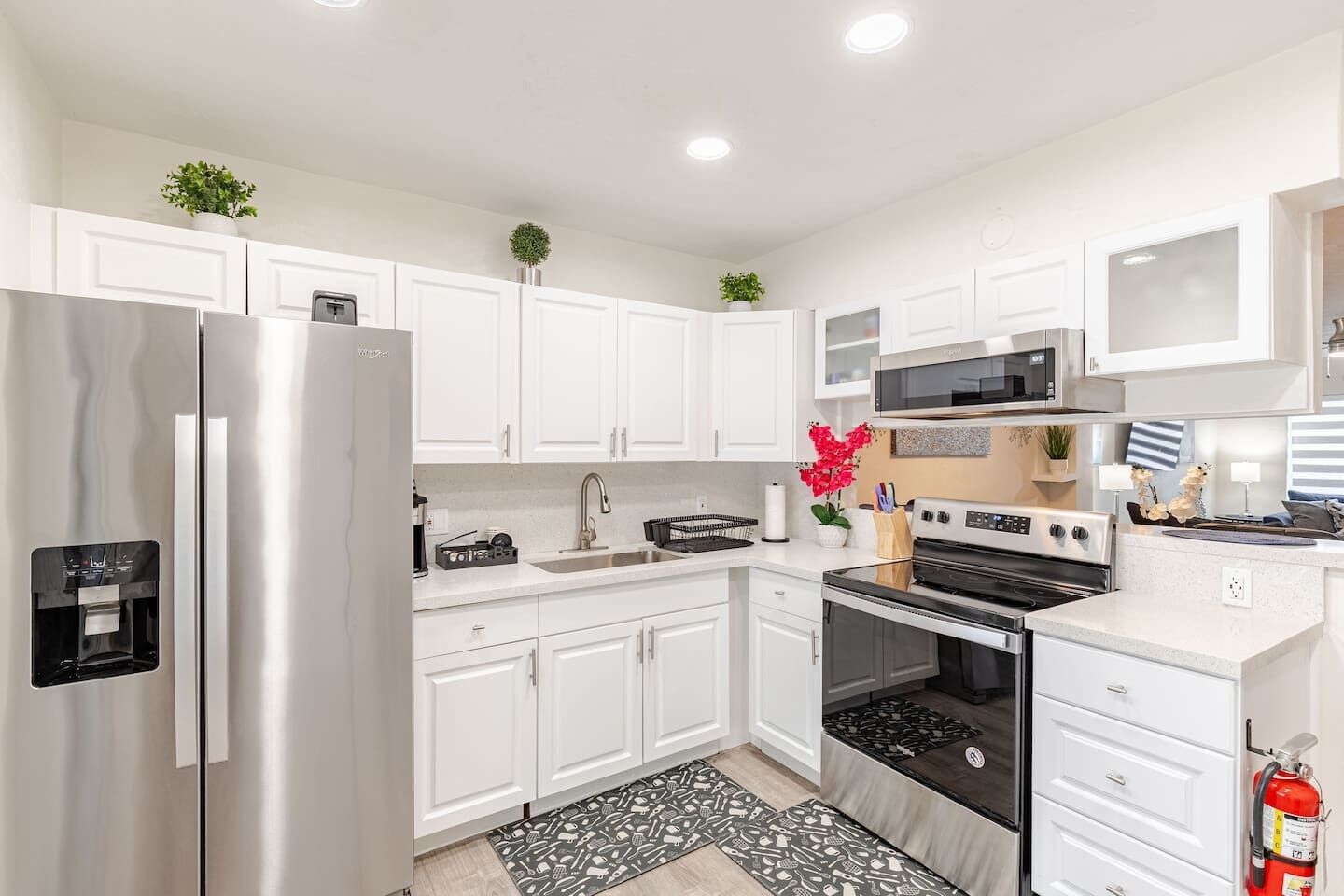 A modern kitchen with white cabinets, stainless steel appliances, and a black and white patterned rug.