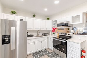 A modern kitchen with white cabinets, stainless steel appliances, and a black and white patterned rug. - Cozy Retreat | Beach, Airport & Cruise Port (Fort Lauderdale)