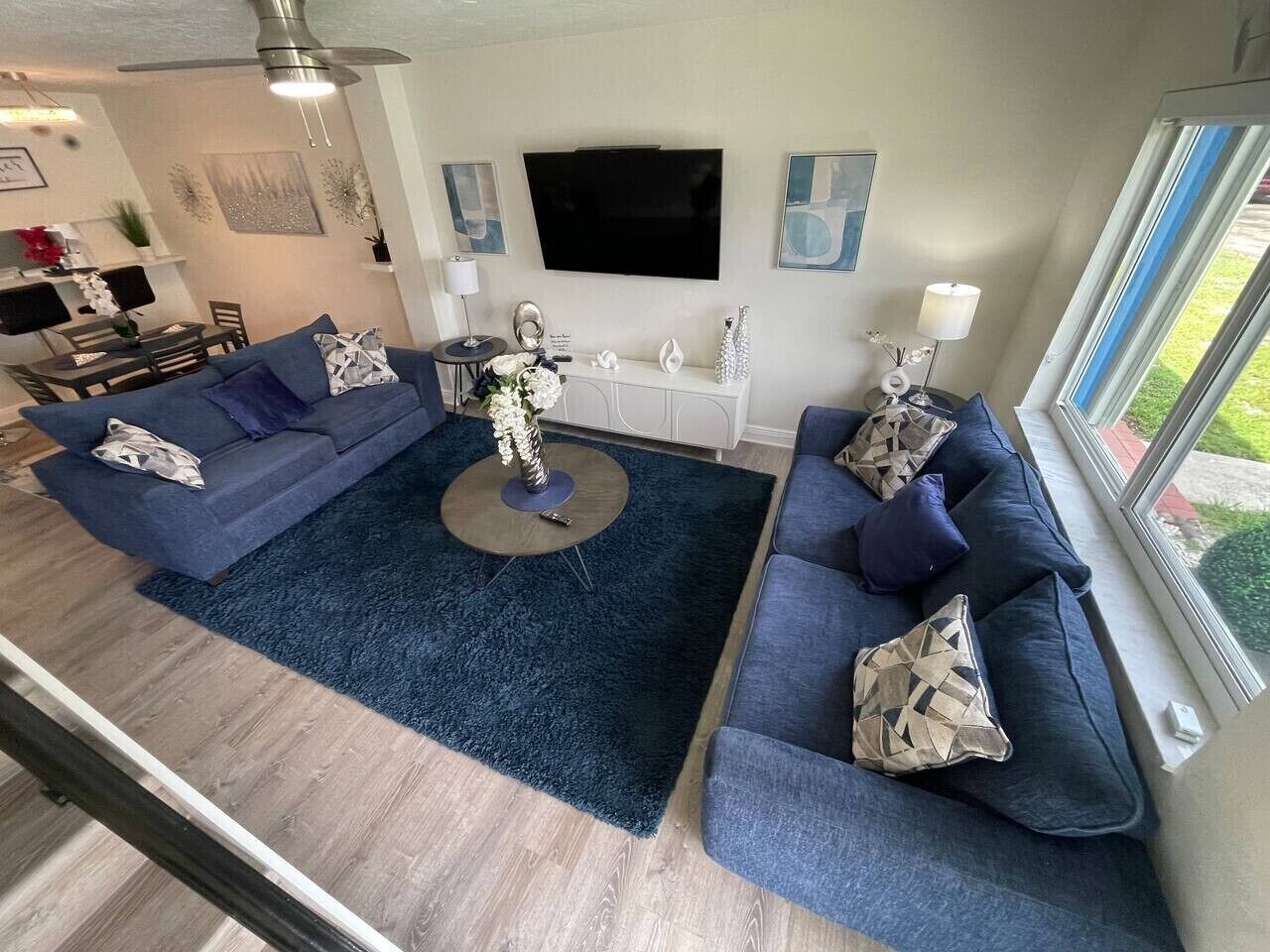 Ein modernes Wohnzimmer mit blauem Teppich, zwei Sofas, einem Couchtisch und einem an der Wand montierten Fernseher.
