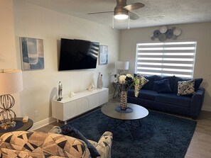 Ein modernes Wohnzimmer mit Flachbildfernseher, einer Couch, einem Couchtisch und dekorativen Accessoires.