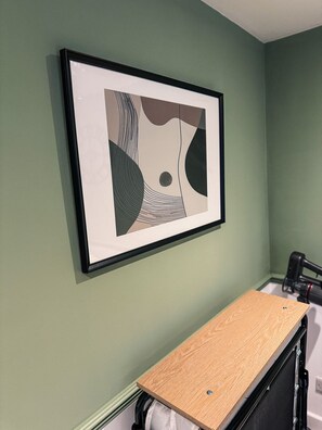 A framed abstract artwork on a wall, a wooden shelf, and a black object on the floor. - Entire rental unit in Berkshire, United Kingdom (Reading)