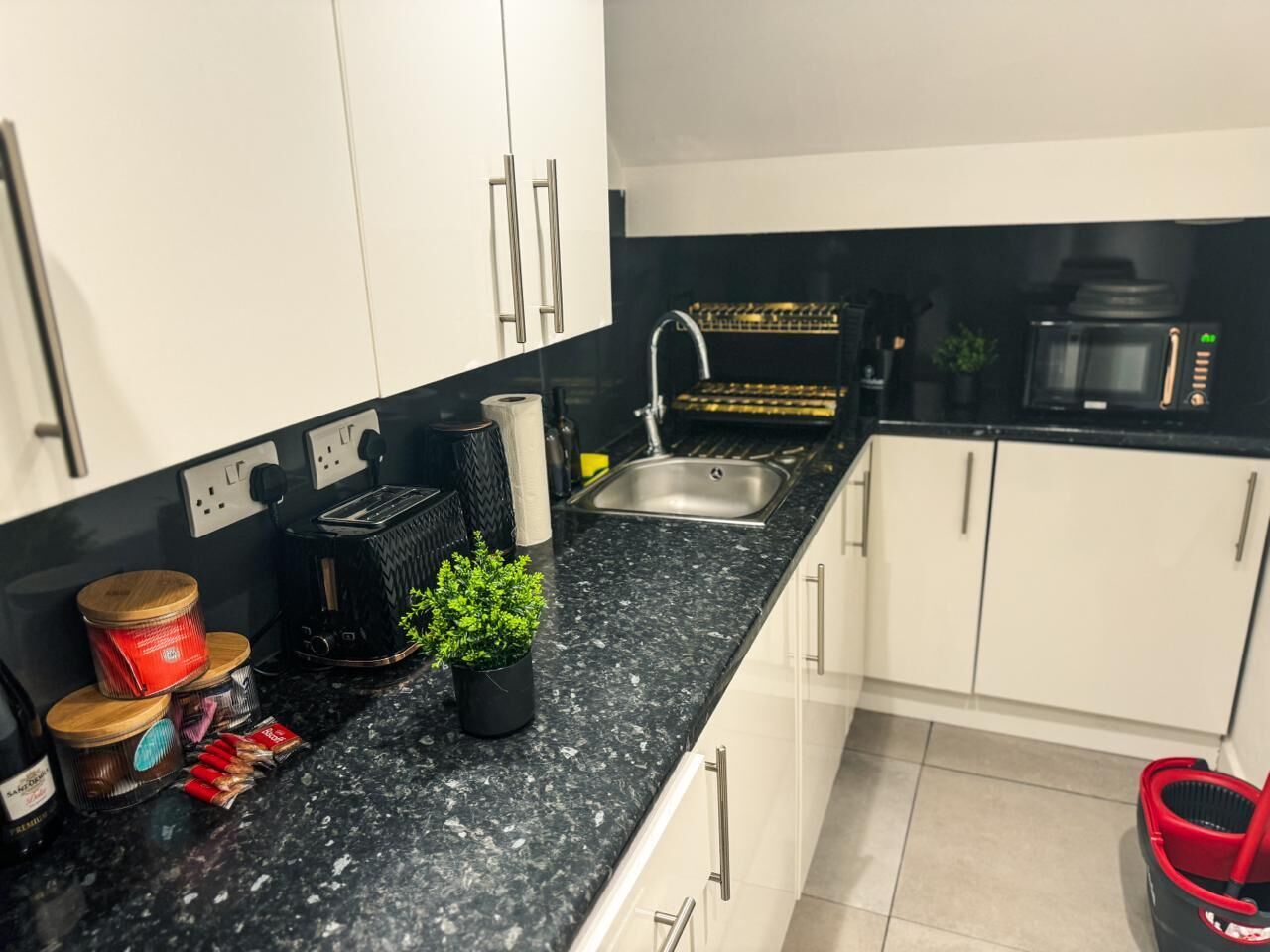 Uma cozinha moderna com armários brancos, bancada de granito preto, pia de aço inoxidável e micro-ondas.