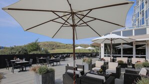 Une terrasse extérieure aménagée avec des meubles en osier, de grands parasols et des plantes en pot.