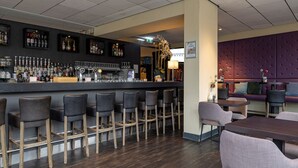 Un espace bar avec des tabourets, un comptoir avec des bouteilles et des verres, et un coin salon avec des tables et des chaises.
