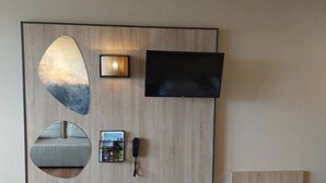 Un téléviseur fixé au mur, un tableau encadré, un miroir rond et une petite table avec un magazine.