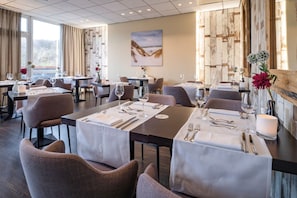 Un restaurant avec plusieurs tables, chacune mise avec des couverts et des verres, et un tableau accroché au mur.