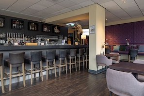 Zona de bar con taburetes, barra con botellas y vasos, y área de estar con mesas y sillas.