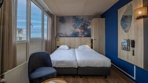 Une chambre d’hôtel avec un lit double, une chaise, une grande fenêtre et un téléphone fixé au mur.
