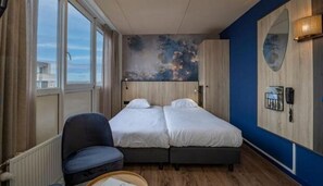 Quarto de hotel com cama de casal, uma cadeira, uma janela grande e telefone fixado na parede.