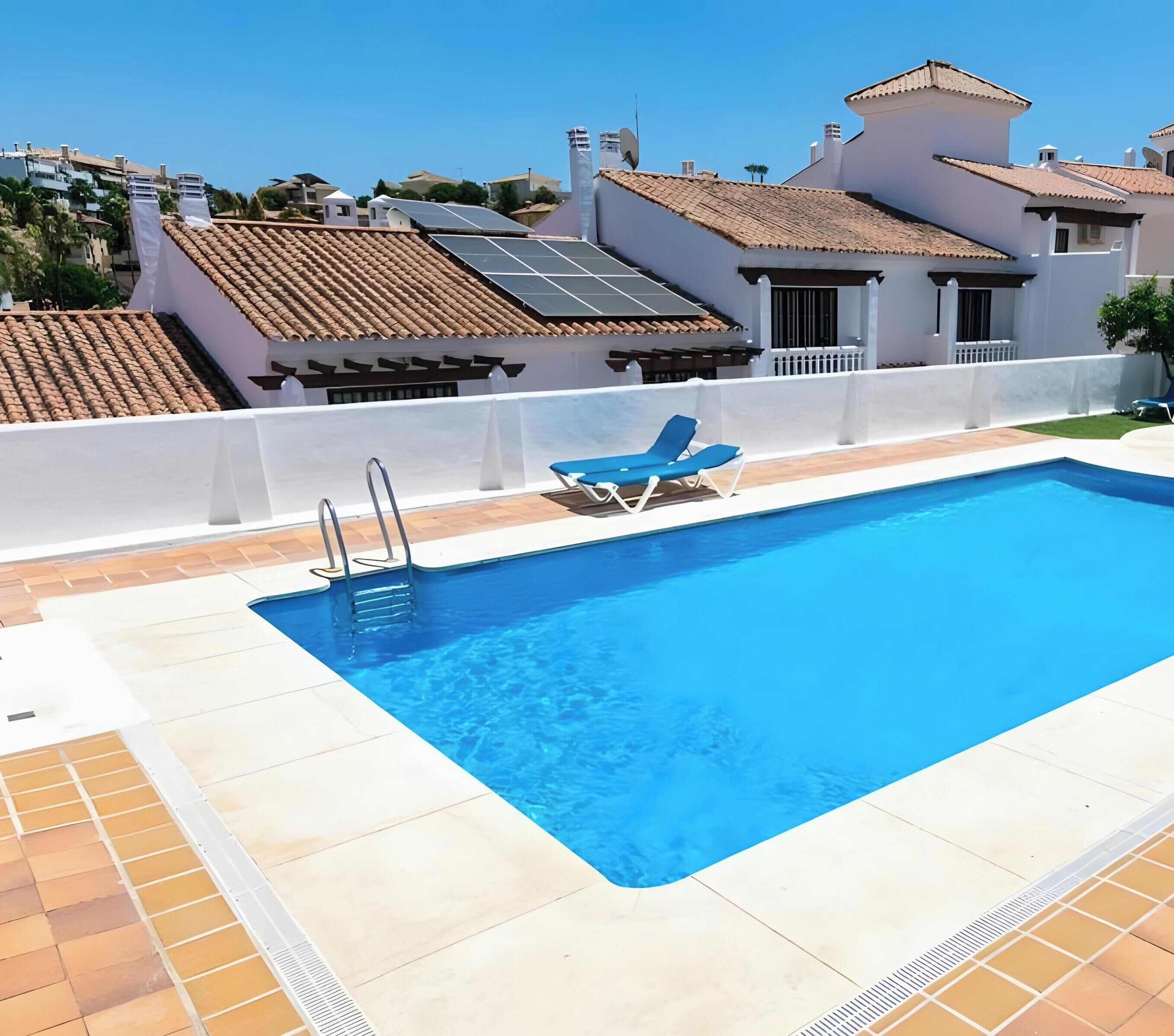 Une piscine à l’eau d’un bleu cristallin, une terrasse carrelée de blanc et un fauteuil de relaxation bleu.