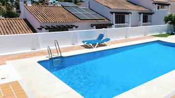 Une piscine à l’eau d’un bleu cristallin, une terrasse carrelée de blanc et un fauteuil de relaxation bleu.