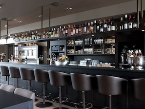 Un espace bar doté de plusieurs tabourets, d’un comptoir avec des bouteilles et des verres, et d’un réfrigérateur.