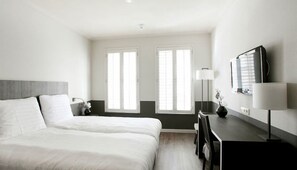 Hotellihuone, jossa on sänky, työpöytä, lamppu ja kaksi ikkunaa.