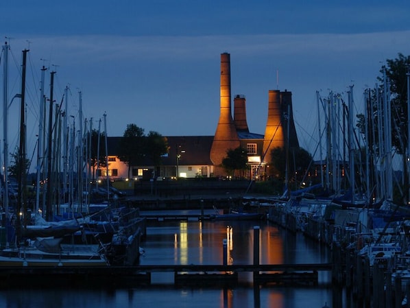 A marina with boats docked, a building with two tall chimneys, and a bridge in the foreground. - Perfect Harbor Stay w/Onsite Dining | Near Huizen Attractions & Nature Reserves (Huizen)