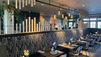 A modern restaurant with a long counter, multiple tables, and a patterned wall.