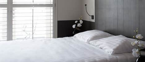 A neatly made bed with white linens, a dark headboard, and a vase with white flowers on a bedside table.