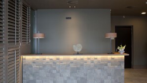 Un comptoir d’accueil avec une façade en pierre à texture, deux lampes fixées au mur et un élément décoratif en verre.
