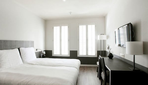 Ein Hotelzimmer mit einem Bett, einem Schreibtisch, einer Lampe und zwei Fenstern.