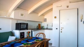 Eine kompakte Küchenzeile mit Mikrowelle, Spüle und kleinem Kühlschrank. Ein Esstisch mit farbenfroher Tischdecke und einem Stuhl sind vorhanden.