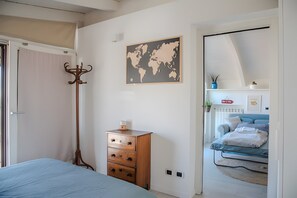 Ein Schlafzimmer mit einem Bett, einer hölzernen Kommode, einer Weltkarte an der Wand und Blick in einen weiteren Raum mit Bett und Regal.