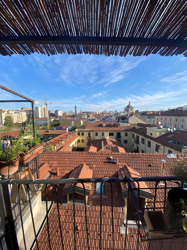 Eine Dachterrasse mit Terrakotta-Fliesen, Blick auf die Stadt und einem strahlend blauen Himmel.