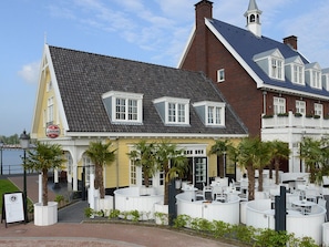 A waterfront hotel with a yellow facade, white-framed windows, and a terrace with outdoor seating. - Serene Stay w/Oniste Dining Near Huizer Museum, Nature Reserve & Cultural Sites (Huizen)