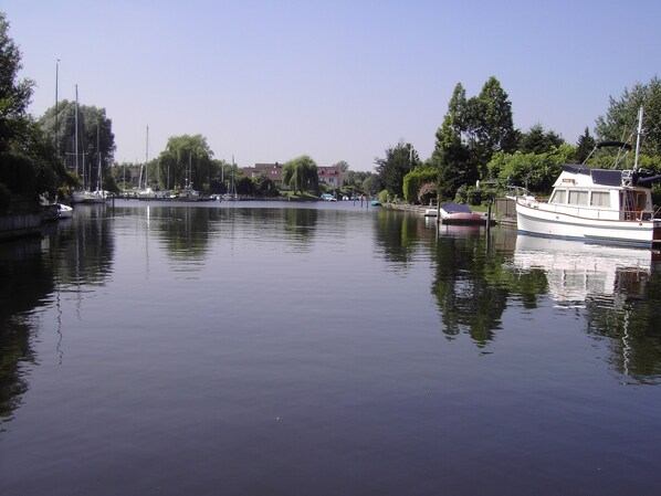 A calm river with boats docked along the shore, surrounded by trees and buildings.
