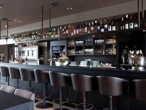 A bar area with multiple stools, a counter with bottles and glasses, and a refrigerator.