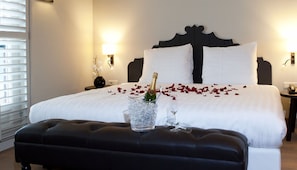 Une chambre d’hôtel avec un grand lit, une table de chevet ornée d’un vase de fleurs et une bouteille de champagne posée sur le lit.
