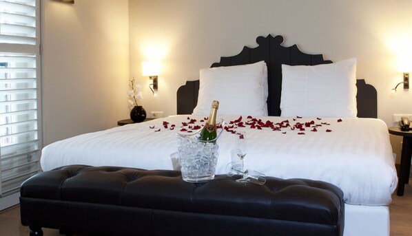 A hotel room with a large bed, a bedside table with a vase of flowers, and a bottle of champagne on the bed. - Explore Huizen in Perfect Suite w/Onsite Dining Near Breathtaking Reserves (Huizen)