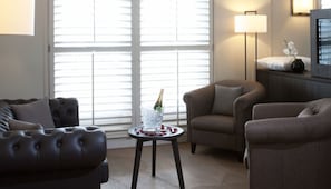 Un salon avec un canapé en cuir marron, une petite table ronde sur laquelle se trouve une bouteille de champagne et une lampe.