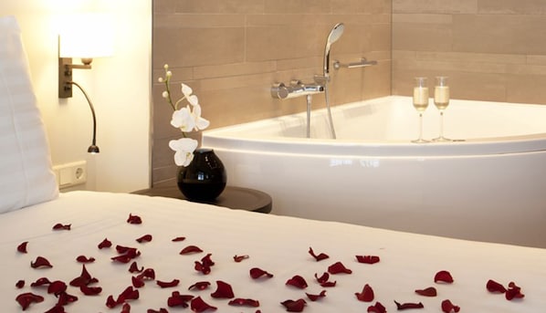 A hotel room with a large bathtub, a bedside table with a vase of white flowers, and rose petals scattered on the bed. - Explore Huizen in Perfect Suite w/Onsite Dining Near Breathtaking Reserves (Huizen)