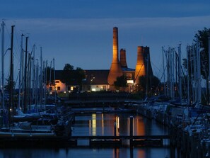 A marina with boats docked, a building with two tall chimneys, and a bridge in the foreground.