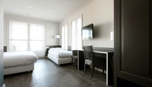 A hotel room with two beds, a desk, and a TV.
