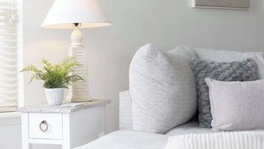 Um quarto com uma cama, uma mesa de cabeceira com abajur, um vaso de planta e um quadro na parede.