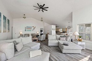 A spacious living area with a modern ceiling fan, a kitchen in the background, and a large window with blinds. - Palencia by the Sea - Ocean & Lighthouse Views (St. Augustine)