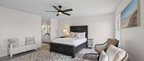 A bedroom with a bed, a chair, a bedside table, a ceiling fan, and a painting on the wall.
