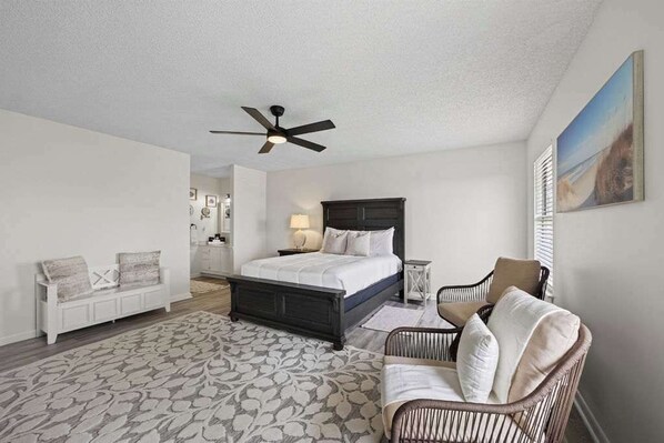 A bedroom with a bed, a chair, a bedside table, a ceiling fan, and a painting on the wall. - Palencia by the Sea - Ocean & Lighthouse Views (St. Augustine)