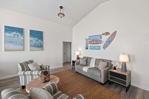 A living room with a sofa, armchairs, a coffee table, and a rug. There are wall art pieces and a decorative sign on the wall. - Palencia by the Sea - Ocean & Lighthouse Views (St. Augustine)