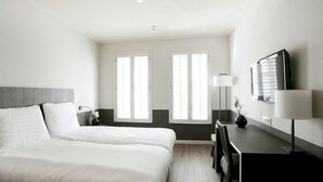Une chambre d’hôtel avec un lit, un bureau, une lampe et deux fenêtres.
