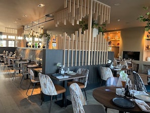 A modern restaurant with wooden decor, multiple dining tables, and chairs.