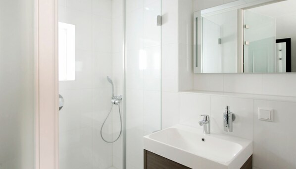 Un baño moderno con cabina de ducha de vidrio, un lavamanos blanco y un espejo sobre él.