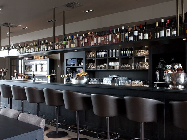 A bar area with multiple stools, a counter with bottles and glasses, and a refrigerator.