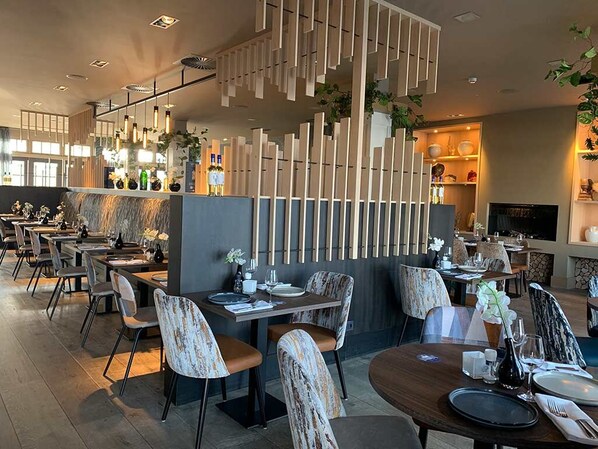 Moderni ravintola, jossa on puusisustus, useita ruokapöytiä ja tuoleja.