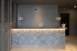 A reception desk with a textured stone facade, two wall-mounted lamps, and a decorative glass piece. - Tranquil Oasis | Soothing Gooimeer Lake & Tafelbergheide Getaway | 2 Units (Huizen)